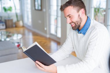 Evde kitap okuyan yakışıklı bir adam.