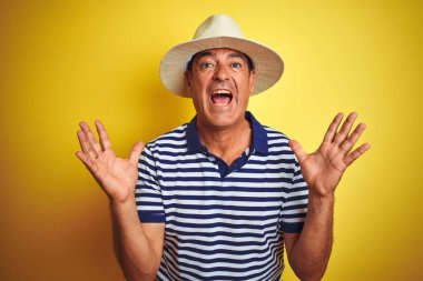 Yakışıklı orta yaş adam izole sarı arka plan deli ve deli bağırarak üzerinde çizgili polo ve şapka giyen ve agresif ifade ve kollar kaldırdı ile bağırıyor. Hayal kırıklığı kavramı.