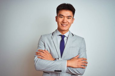 Çıplak beyaz arka plan üzerinde ayakta gri ceket ve kravat giyen Asya Çinli işadamı fotoğraf makinesi bakarak çapraz silah ile gülümseyen yüz. Pozitif kişi.