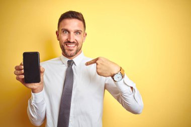 Sürpriz yüz kendisini işaret parmak ile sarı izole arka plan üzerinde akıllı telefon ekranı gösteren genç yakışıklı iş adamı