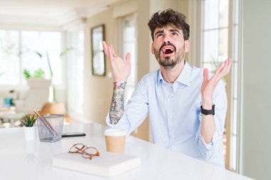 Genç iş adamı deli ve deli çığlık ve agresif ifade ve silah ile bağırarak çalışıyor kaldırdı. Hayal kırıklığı kavramı.