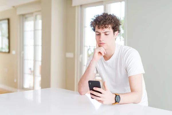 Jonge Man Met Smartphone Thuis Serieus Gezicht Denken Vraag Zeer — Stockfoto