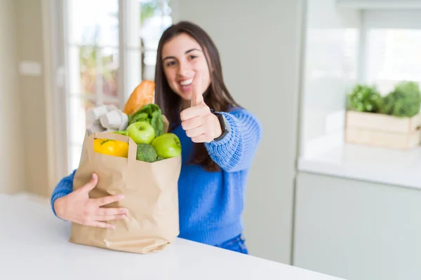 健康的な食料品でいっぱいの紙袋を持つ美しい若い女性は Okサインをやって大きな笑顔で幸せ 指で親指アップ 優れた看板 — ストック写真