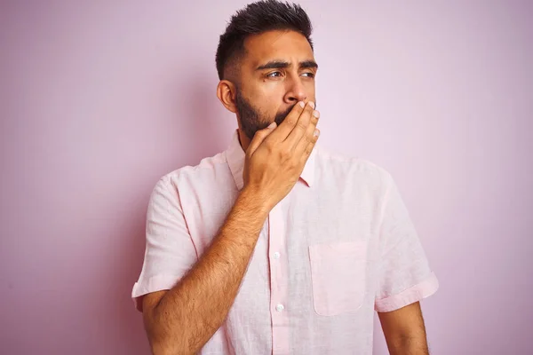 Young indian man wearing casual shirt standing over isolated pink background bored yawning tired covering mouth with hand. Restless and sleepiness.