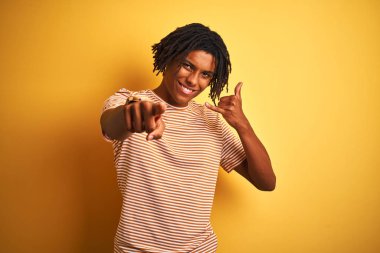 Kıvırcık sarı arka plan üzerinde ayakta çizgili t-shirt giyen dreadlocks ile Afro adam telefon jest konuşurken ve size işaret ediyor. Beni ara.