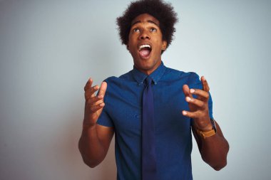 Afro saç ile Amerikan iş adamı mavi gömlek giyiyor ve izole beyaz arka plan üzerinde kravat deli ve deli çığlık ve agresif ifade ve silah ile bağırdı kaldırdı. Hayal kırıklığı kavramı.