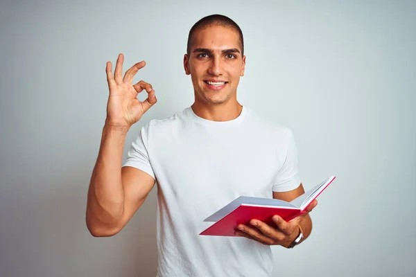 年轻的帅哥读红书在白色孤立的背景做好标志用手指 优秀的符号 — 图库照片