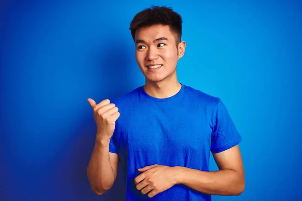 孤立した青い背景の上に立つTシャツを着た若いアジア人の男性は 幸せそうな顔で微笑み 親指を上げて横を向いている — ストック写真