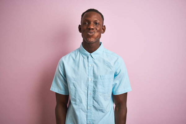 African american man wearing blue casual shirt standing over isolated pink background puffing cheeks with funny face. Mouth inflated with air, crazy expression.