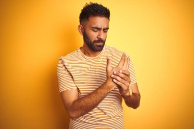 Genç Hint adam giyen t-shirt ayakta üzerinde izole sarı arka plan eller ve parmaklarda acı acı, artrit iltihabı