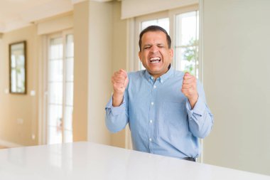 Evde oturan orta yaş adam silah ile başarı için heyecanlı gülümseme kutluyor kaldırdı. Kazanan kavramı.