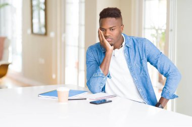 Dizüstü bilgisayar kullanarak okuyan ve kulaklık giyen Afrikalı Amerikalı öğrenci adam yorgun bakıyor ve çapraz silah ile depresyon sorunları ile sıkılmış düşünme.