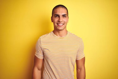 Yüzünde mutlu ve serin bir gülümseme ile sarı izole arka plan üzerinde çizgili t-shirt giyen genç yakışıklı adam. Şanslı kişi.