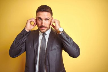 Sarı izole arka plan üzerinde genç yakışıklı iş adamı gürültülü müzik gürültü için rahatsız ifade ile parmaklar ile kulakları kaplayan. Sağır kavramı.