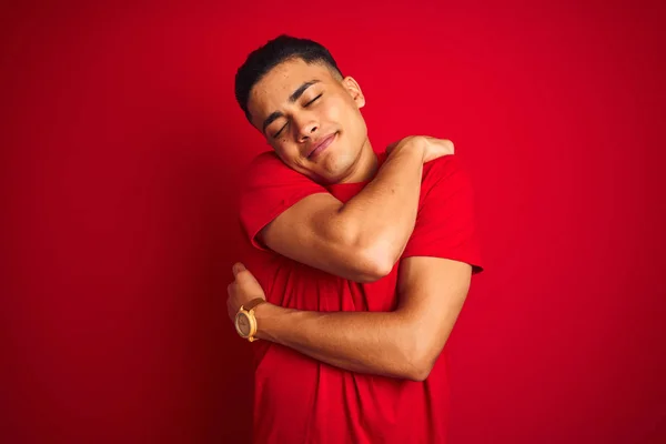 Jovem Brasileiro Vestindo Camiseta Sobre Fundo Vermelho Isolado Abraçando Feliz — Fotografia de Stock