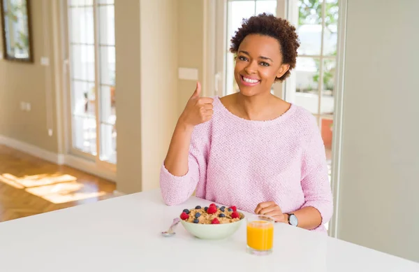 年轻的非洲裔美国妇女早上在家吃健康早餐 用手做快乐的竖起大拇指手势 批准显示显示成功的相机的表达式 — 图库照片