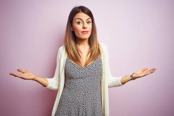 Genç güzel kadın pembe izole arka plan üzerinde duran habersiz ve açık kollar ile karışık, hiçbir fikir kavramı.
