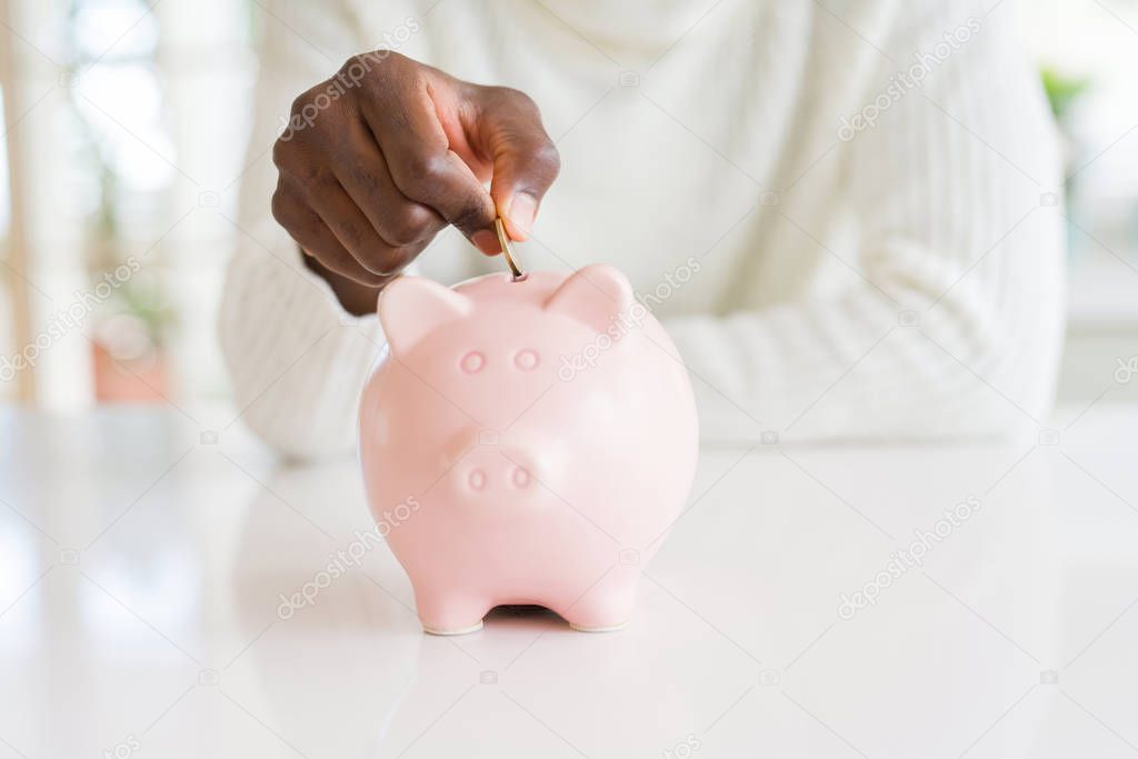 Close up of african man hands putting a coin inside piggy bank, saving money as investment