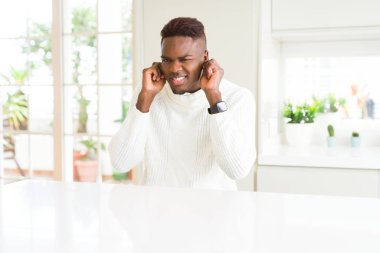 Beyaz masada yakışıklı Afrikalı Amerikalı adam yüksek sesle müzik gürültü için rahatsız ifade ile parmaklarıyla kulakları kapsayan. Sağır kavramı.