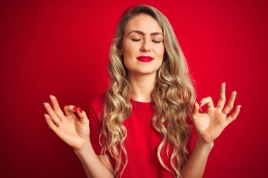 Kırmızı izole arka plan üzerinde ayakta temel t-shirt giyen genç güzel kadın Relax ve gözleri ile gülümseyen meditasyon jest parmaklar ile kapalı. Yoga konsepti.