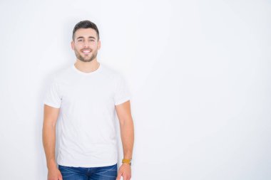 Beyaz izole arka plan üzerinde rahat beyaz t-shirt giyen mutlu gülümseyen genç yakışıklı adam