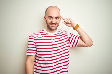 Beyaz izole arka plan üzerinde rahat çizgili kırmızı t-shirt giyen sakal ile genç kel adam bir parmak ile kafa işaret gülümseyen, harika bir fikir veya düşünce, iyi bellek