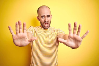 Sakal ile genç kel adam rahat çizgili t-shirt sarı izole arka plan üzerinde eller avuç içi, öfkeli ve hayal kırıklığı ifade ile stop jest yapıyor