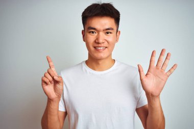 Genç Asyalı Çinli adam izole beyaz arka plan üzerinde ayakta t-shirt giymiş ve parmak numarası altı ile işaret kadar emin ve mutlu gülümseyen.