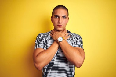 Sarı izole arka plan üzerinde çizgili t-shirt giyen genç yakışıklı adam çığlık ve ağrılı boğma çünkü boğulmak. Sağlık problemi. Asphyxiate ve intihar konsepti.