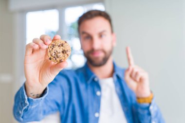 Çerezler bir fikir ya da soru işaret parmağı gülen yüz, bir numara ile sürpriz yakışıklı adam yeme çikolata cips