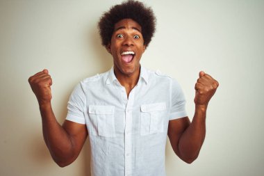 Afro saç ile Afrikalı Amerikan adam izole beyaz arka plan üzerinde ayakta gömlek giymiş sürpriz kutluyor ve başarı için hayran silah kaldırdı ve açık gözleri ile. Kazanan kavramı.