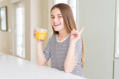 Taze portakal suyu bir bardak içme güzel genç kız çocuk çok mutlu yan el ve parmak ile işaret
