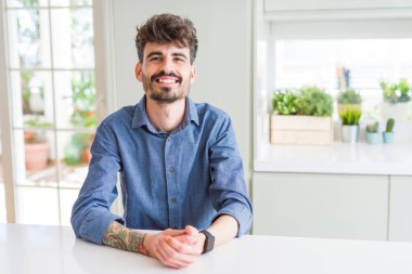 Genç adam rahat gömlek beyaz masa ellerde birlikte oturan ve parmak giyiyor rahat ve neşeli gülümseyen geçti. Başarı ve iyimser