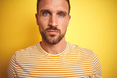 Yakın yüzünde ciddi ifade ile sarı izole arka plan üzerinde rahat t-shirt giyen genç yakışıklı adam. Kameraya basit ve doğal bir bakış.