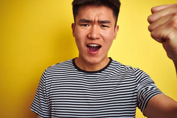年轻的亚洲中国男子穿着条纹T恤站在孤立的黄色背景恼火和沮丧的喊叫与愤怒 疯狂和大喊大叫与举手 愤怒的概念 — 图库照片