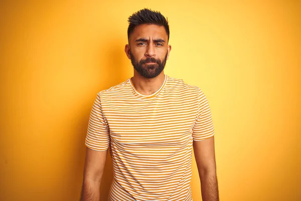 Young indian man wearing t-shirt standing over isolated yellow background depressed and worry for distress, crying angry and afraid. Sad expression.