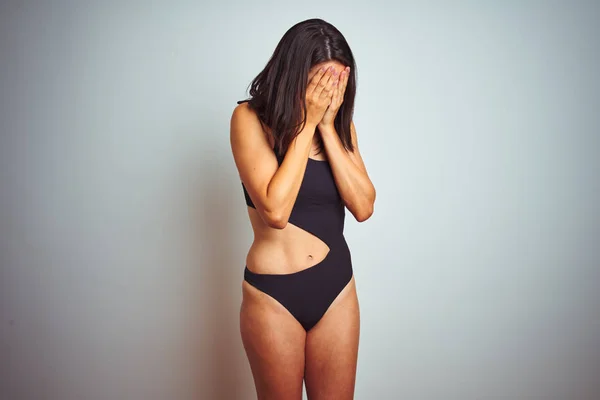 Beautiful woman wearing bikini swimwear over white isolated background with sad expression covering face with hands while crying. Depression concept.