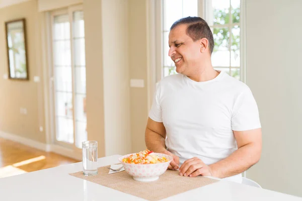 Middle age man eating rice at home looking away to side with smile on face, natural expression. Laughing confident.