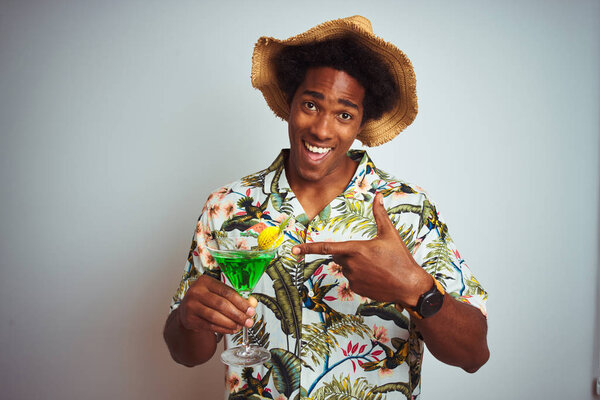 Афро человек на праздники носить летнюю шляпу пить коктейль на изолированном белом фоне очень счастливы указывая рукой и пальцем

