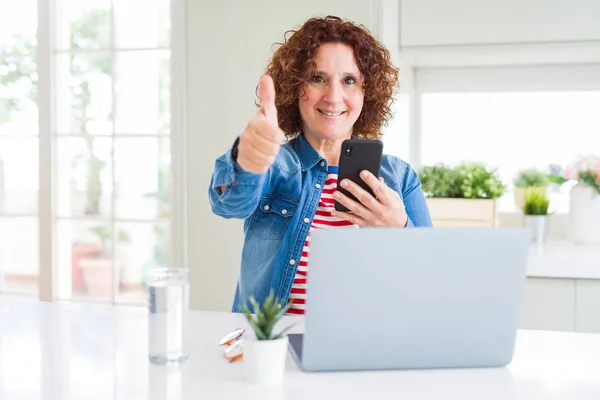 ノートパソコンやスマホを使うシニア女性は Okサインをやって大きな笑顔で幸せ 指で親指アップ 優れたサイン — ストック写真