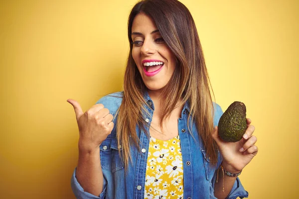 Jovem Mulher Bonita Comendo Abacate Saudável Sobre Fundo Amarelo Apontando — Fotografia de Stock