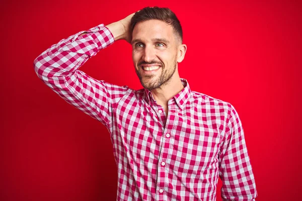 Genç yakışıklı adam üzerinde kırmızı izole arka plan gülümseyen emin dokunuşlu saç el yukarı jest ile çekici ve moda