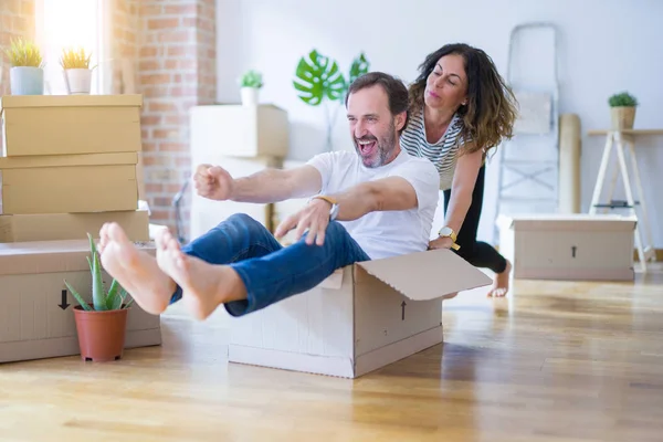 Middle age senior romantic couple having fun riding inside of cardboard, excited and smiling happy for moving to a new home