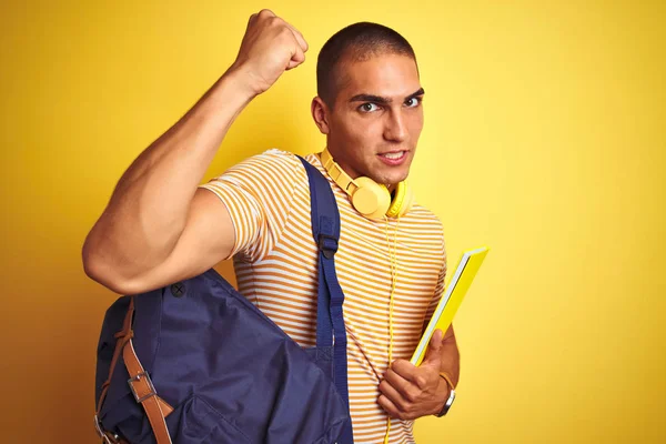 年轻学生男子戴着耳机和背包在黄色孤立的背景恼火和沮丧的喊叫与愤怒 疯狂和大喊大叫与举手 愤怒的概念 — 图库照片