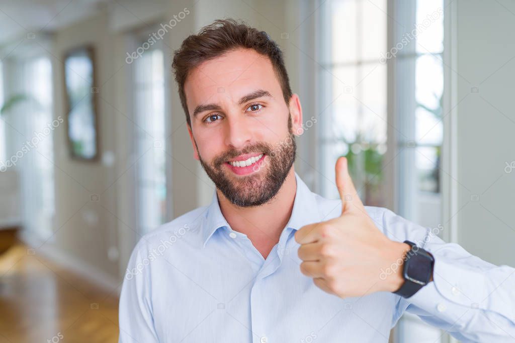 Handsome business man doing happy thumbs up gesture with hand. Approving expression looking at the camera with showing success.