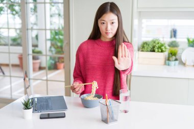 Güzel Asyalı kadın laptop kullanarak çalışan ve açık el ile Asya Erişte yeme ciddi ve emin ifade ile stop işareti yapıyor, savunma jest
