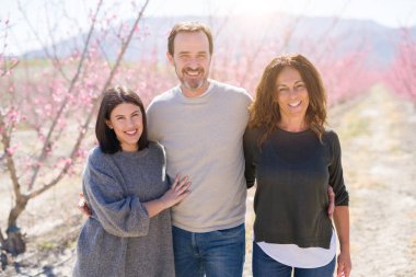 Üç neşeli yürüyüş toghether şeftali bahçesinde bahar güneşli gün zevk pembe yaprakları ile gülümseyen güzel aile