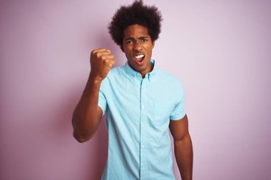 Afro saç ile genç Amerikalı adam mavi gömlek ayakta izole pembe arka plan kızgın ve deli yükseltme yumruk sinirli ve öfkeli çığlık sırasında öfke ile. Öfke ve agresif kavram.
