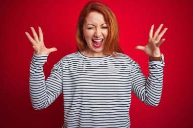 Genç Redhead kadın giyen strapes Lacivert gömlek ayakta kırmızı izole arka plan ile çılgın kutluyor ve başarı için deli silah ile yükseltilmiş ve kapalı gözleri heyecanlı çığlık. Kazanan kavramı