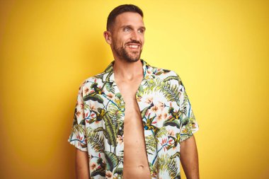 Sarı izole arka planda yaz Hawaii çiçekler gömlek giyen yakışıklı adam yüz, doğal ifade gülümseme ile kenara bakıyor. Güven gülüyor.